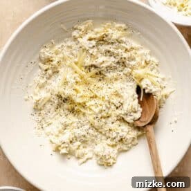 Dried basil, heavy cream, and half of the three cheeses in a large bowl, ready to be mixed into a creamy sauce base with a wooden spoon.