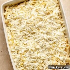 Three cheese mac and cheese in a white rectangular baking dish with an even layer of mixed shredded cheese sprinkled on top, ready for the oven.