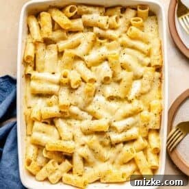 Baked three cheese mac and cheese presented in a white baking pan, showcasing its perfect golden-brown crust and bubbly interior, next to small plates and gold forks for serving.