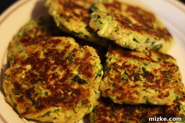 Golden Zucchini Fritters 2 Golden brown zucchini cakes stacked on a plate, garnished with fresh herbs.