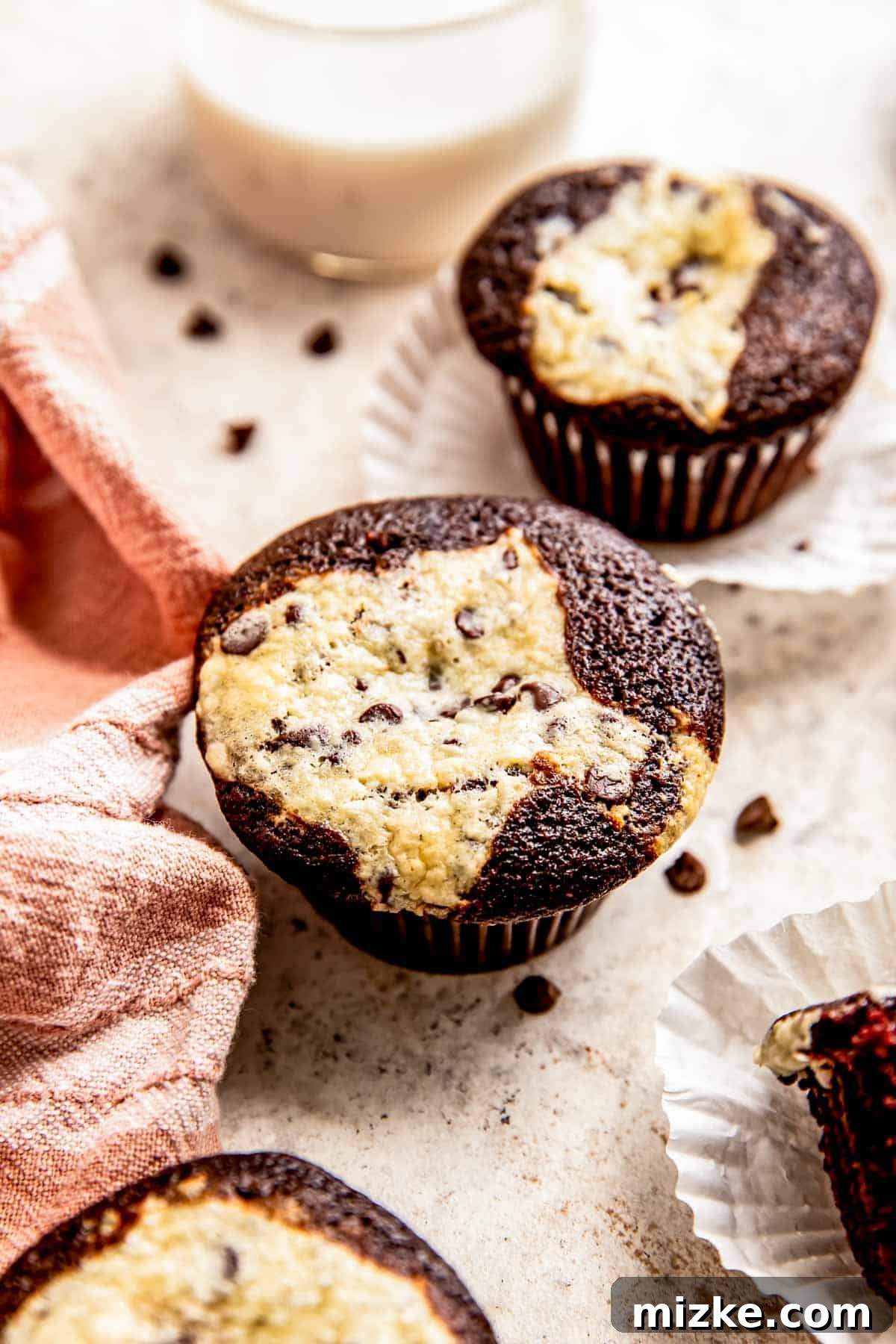 Decadent Chocolate Cream Cheese Cupcakes 3 A perfectly baked individual chocolate cream cheese cupcake resting on a grey surface, with another cupcake subtly blurred in the background, showcasing its delicious texture and filling.