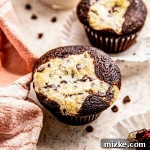 A close-up of a chocolate cream cheese cupcake on a grey background, highlighting its rich filling and moist texture.
