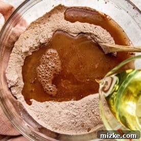 Vegetable oil being poured into a bowl containing flour and cocoa powder, demonstrating the gentle mixing of wet and dry ingredients for the chocolate cupcake batter.