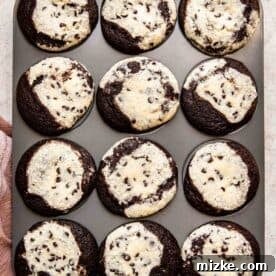 A muffin pan filled with freshly baked chocolate cream cheese cupcakes, with their tops slightly sunken, indicating they are cooling after baking.
