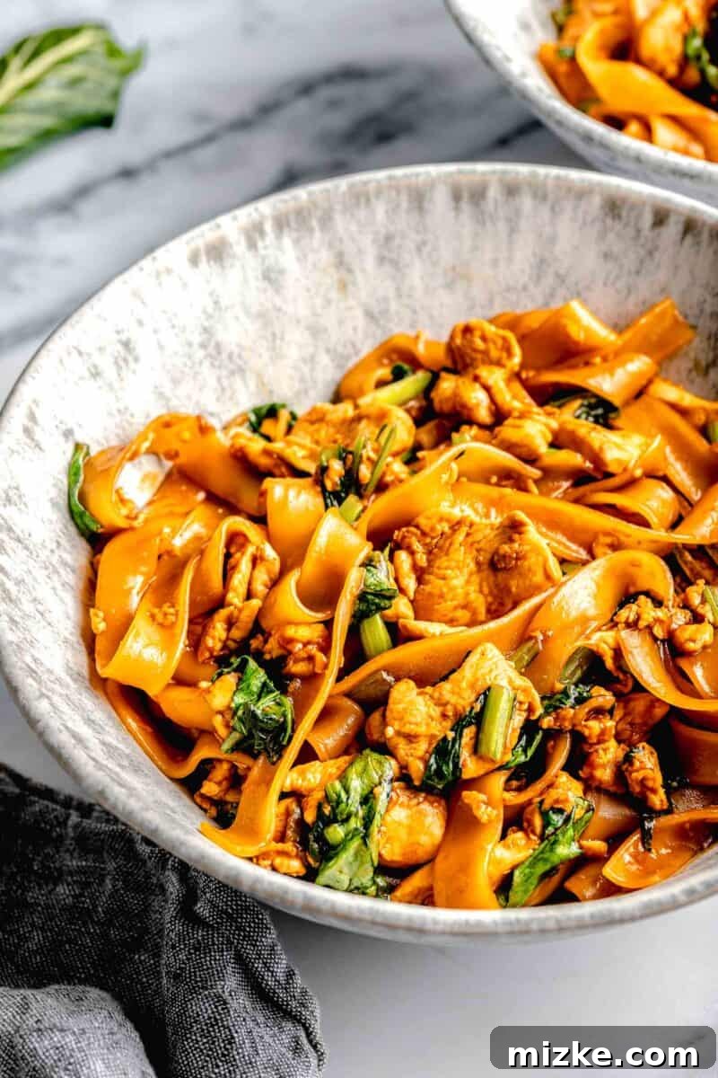 A deep noodle bowl filled with steaming Pad See Ew, ready to be enjoyed, accompanied by a gray towel.