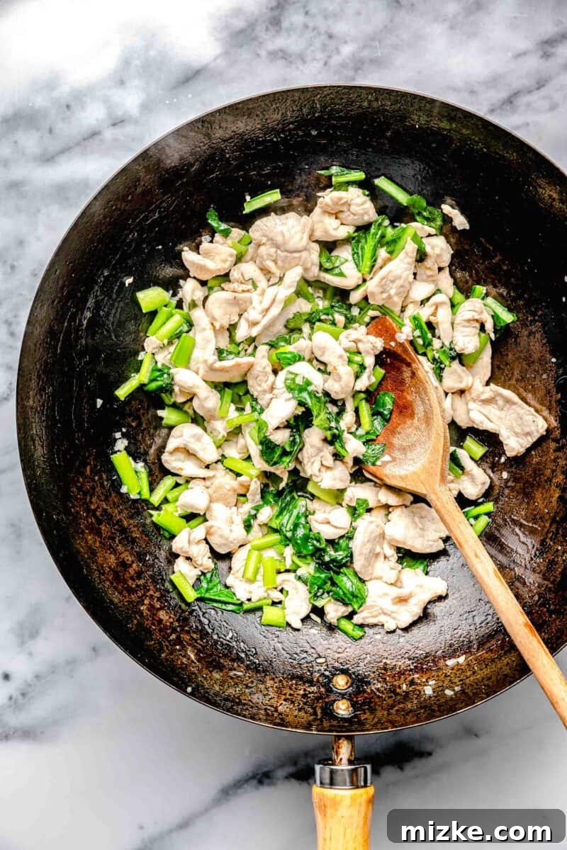 Chicken and Chinese broccoli (Gai Lan) being stir-fried in a hot wok with a wooden spoon.