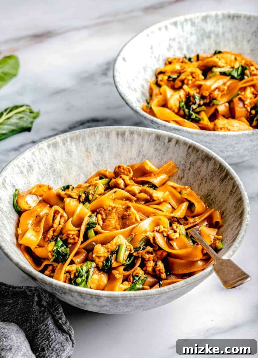 A large deep noodle bowl filled with hot Pad See Ew, featuring a fork ready to pick up the savory noodles.