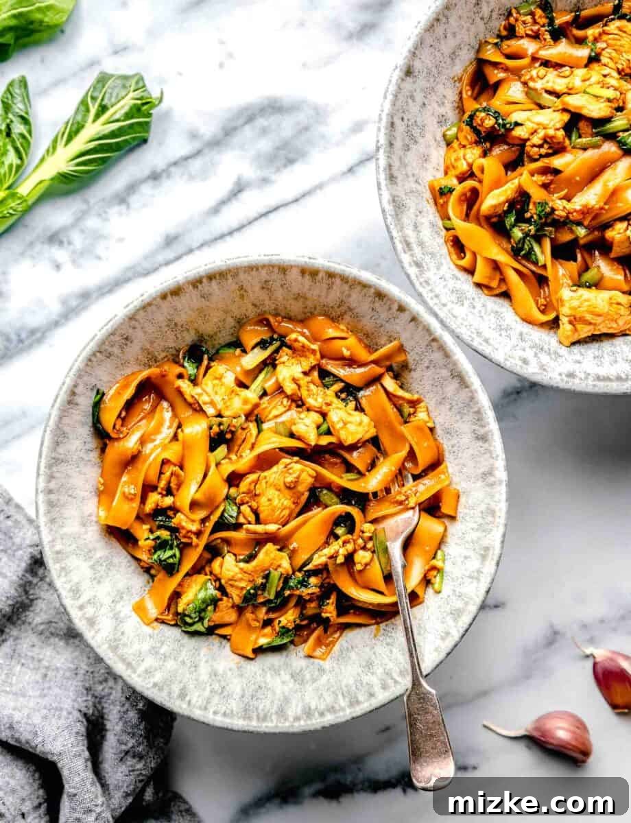 An overhead view of two bowls of Pad See Ew, with a fork in one, showcasing the rich colors and textures of the dish.