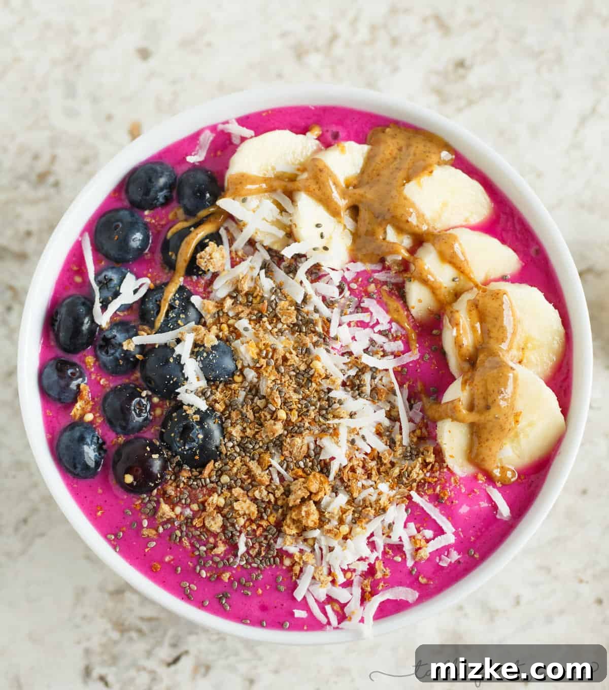 Vibrant Pitaya Breakfast Bowl 2 Vibrant pink pitaya smoothie bowl topped with fresh blueberries, sliced bananas, creamy almond butter, shredded coconut, and crunchy granola. A perfect healthy breakfast.