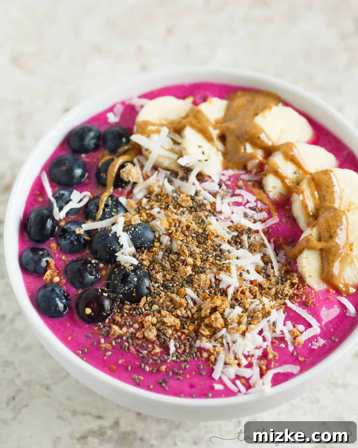 Vibrant Pitaya Breakfast Bowl 3 A closer view of a delicious pitaya smoothie bowl, beautifully arranged with fresh blueberries, banana slices, a swirl of almond butter, crunchy granola, and delicate coconut flakes.