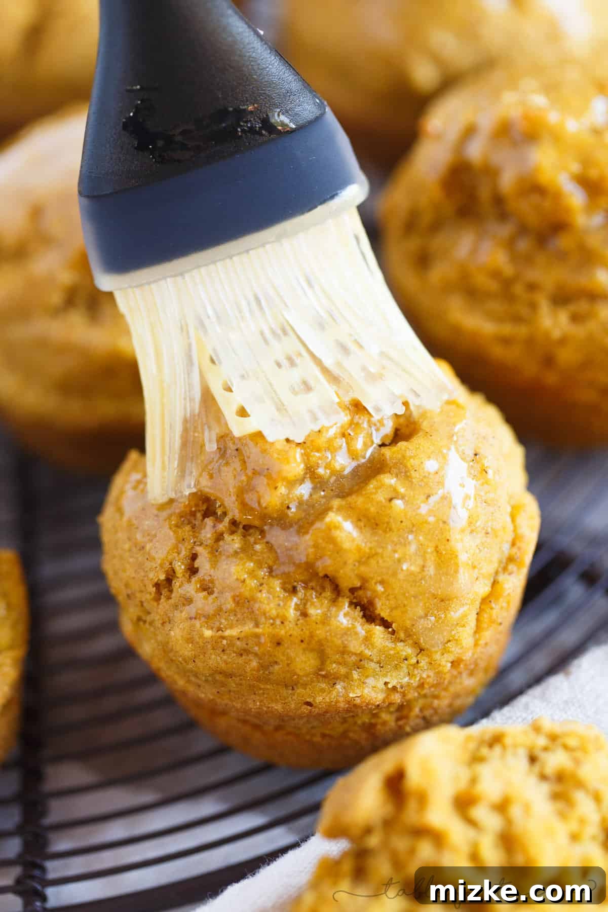 Autumn Spiced Pumpkin Cornbread Muffins 4 A hand gently brushing a warm, freshly baked Pumpkin Cornbread Muffin with creamy, golden maple butter, enhancing its inviting aroma.