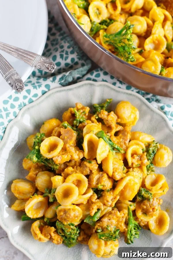 Golden Pumpkin Mascarpone Orecchiette with Zesty Sausage and Broccolini 4 A close-up of a fork lifting some orecchiette pasta from a bowl, highlighting the creamy pumpkin sauce and bits of spicy sausage and broccolini.