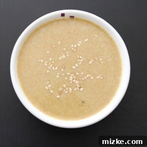 A bowl of creamy homemade tahini sauce, garnished with a vibrant drizzle of olive oil and a sprinkle of paprika, hinting at its potential use in various dishes.