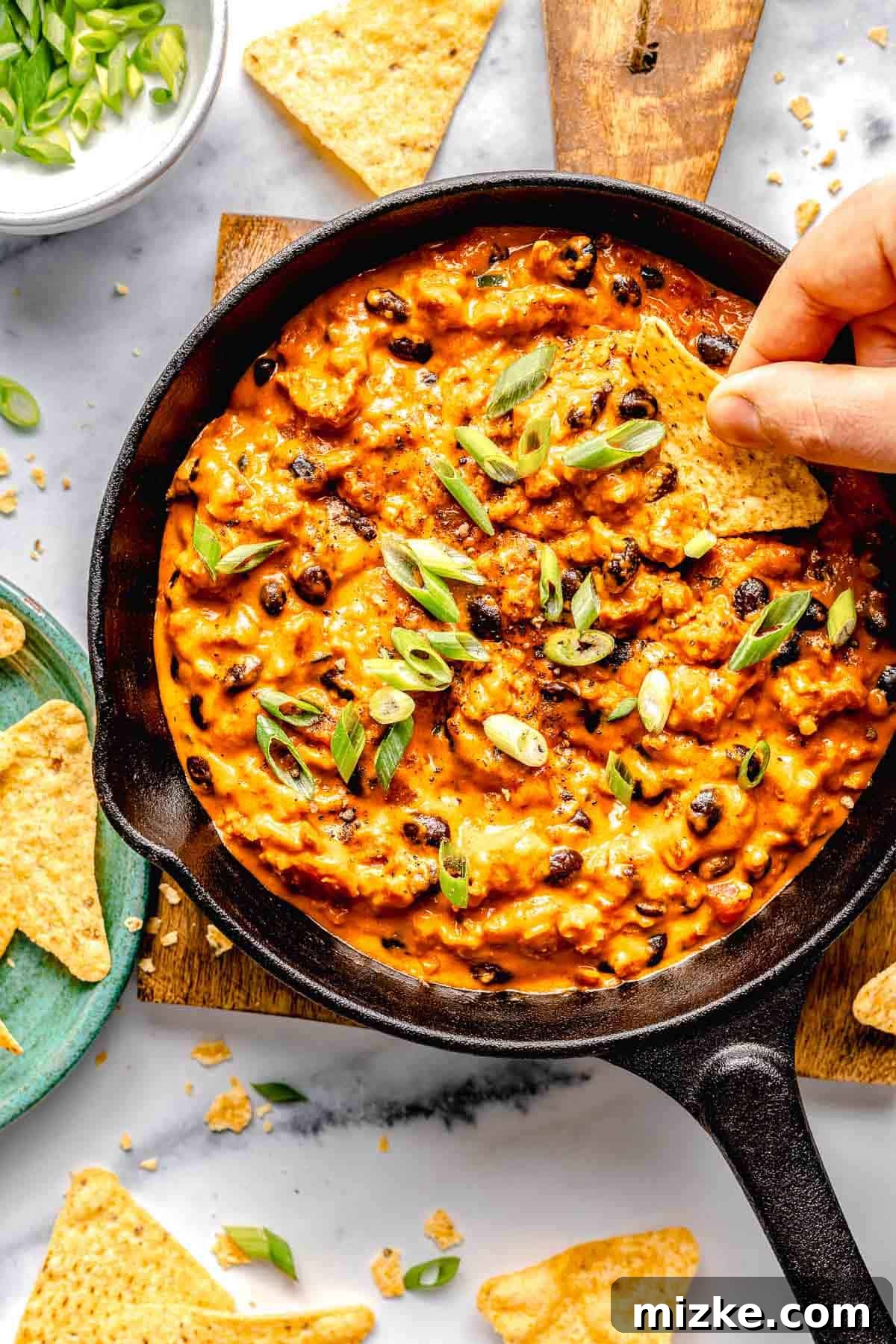 Easy to make and a bit too easy to eat, chili cheese dip is creamy, cheesy, and just the right amount of spicy from the chorizo and jalapeno. Overhead image of scooping a bite of chili cheese dip out of a skillet with a tortilla chip.