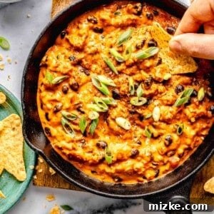 Overhead image of scooping a bite of chili cheese dip out of a skillet with a tortilla chip.