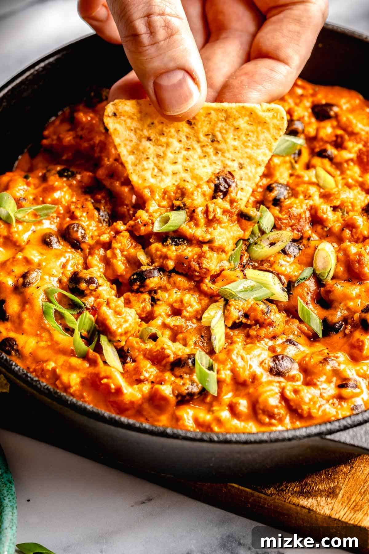 Easy to make and a bit too easy to eat, chili cheese dip is creamy, cheesy, and just the right amount of spicy from the chorizo and jalapeno. Scooping a bite of chili cheese dip out of a skillet with a tortilla chip.