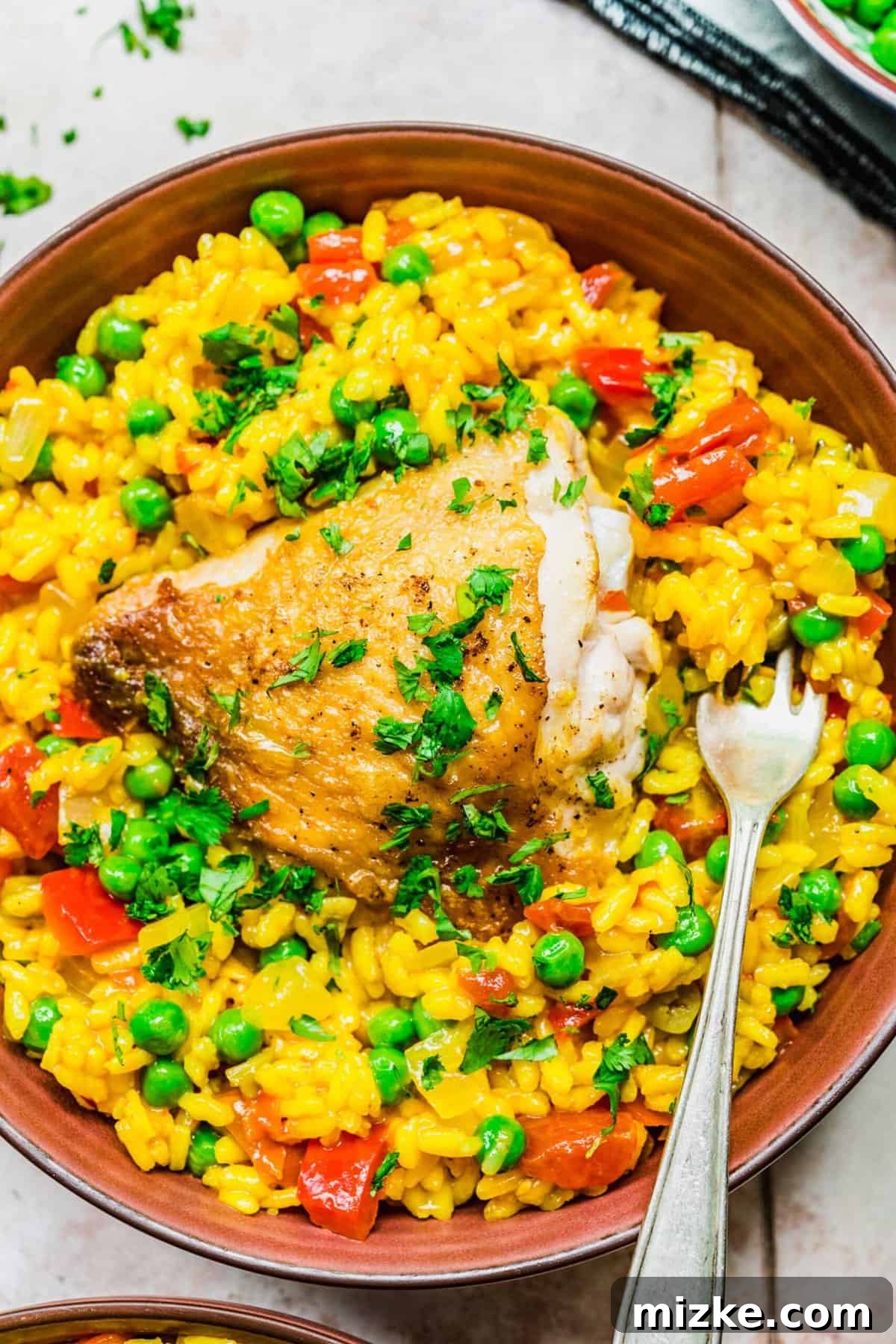 A close-up of a delicious serving of Arroz con Pollo. Overhead view of a serving of Arroz con Pollo in a rustic bowl, with a fork digging into a tender piece of chicken and perfectly cooked rice, ready to be enjoyed.