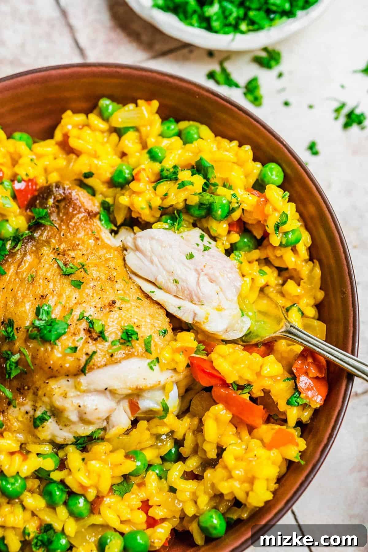 A forkful of Arroz con Pollo, highlighting tender chicken and flavorful rice. Close-up overhead shot of a fork lifting a perfect bite of Arroz con Pollo, showcasing tender chicken, saffron-infused rice, and green olives.