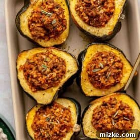 Baked stuffed acorn squash halves filled with rice mixture arranged neatly in a baking dish.