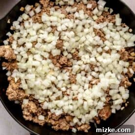 A pan with cooked ground sausage topped with a layer of diced onions.