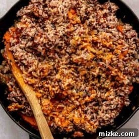 A skillet filled with cooked wild rice mixed with pumpkin, accompanied by a wooden spoon.