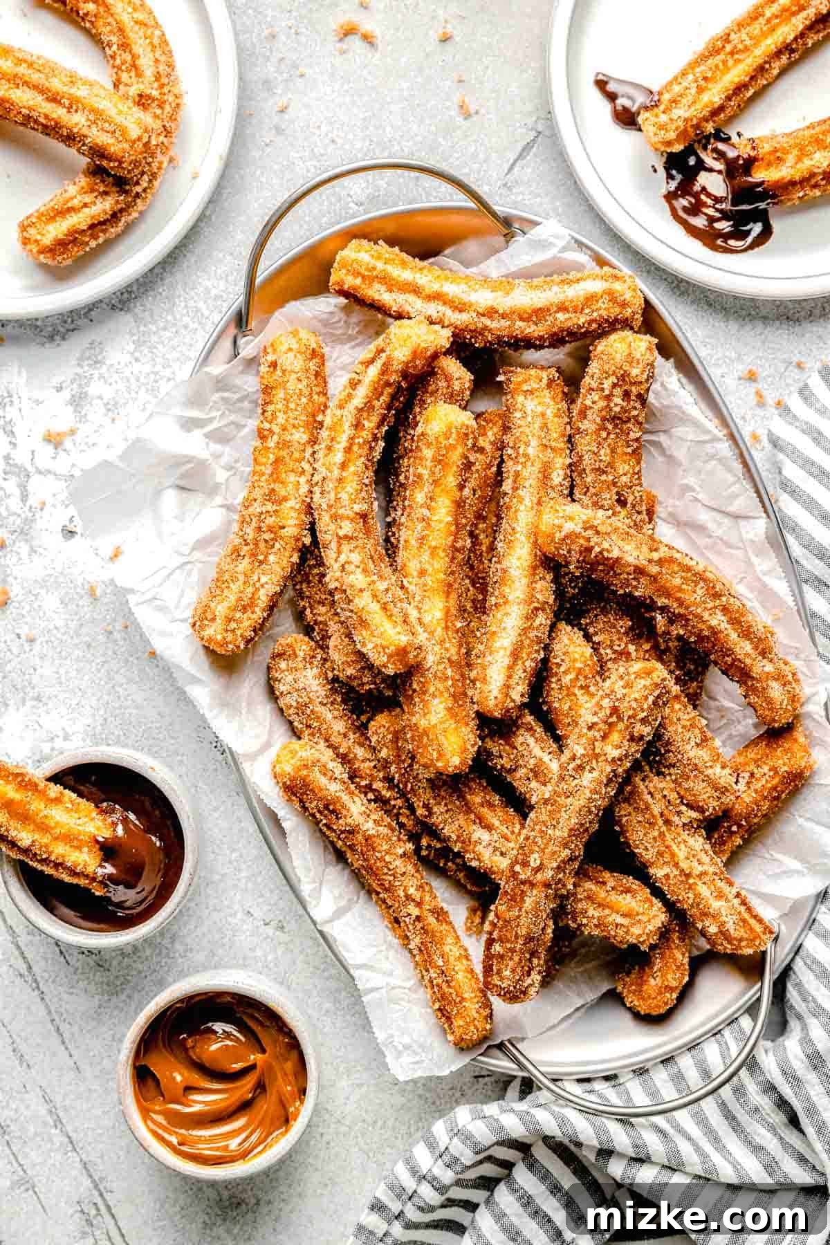 mexican churros on a metal platter with parchment paper next to caramel sauce and chocolate sauce