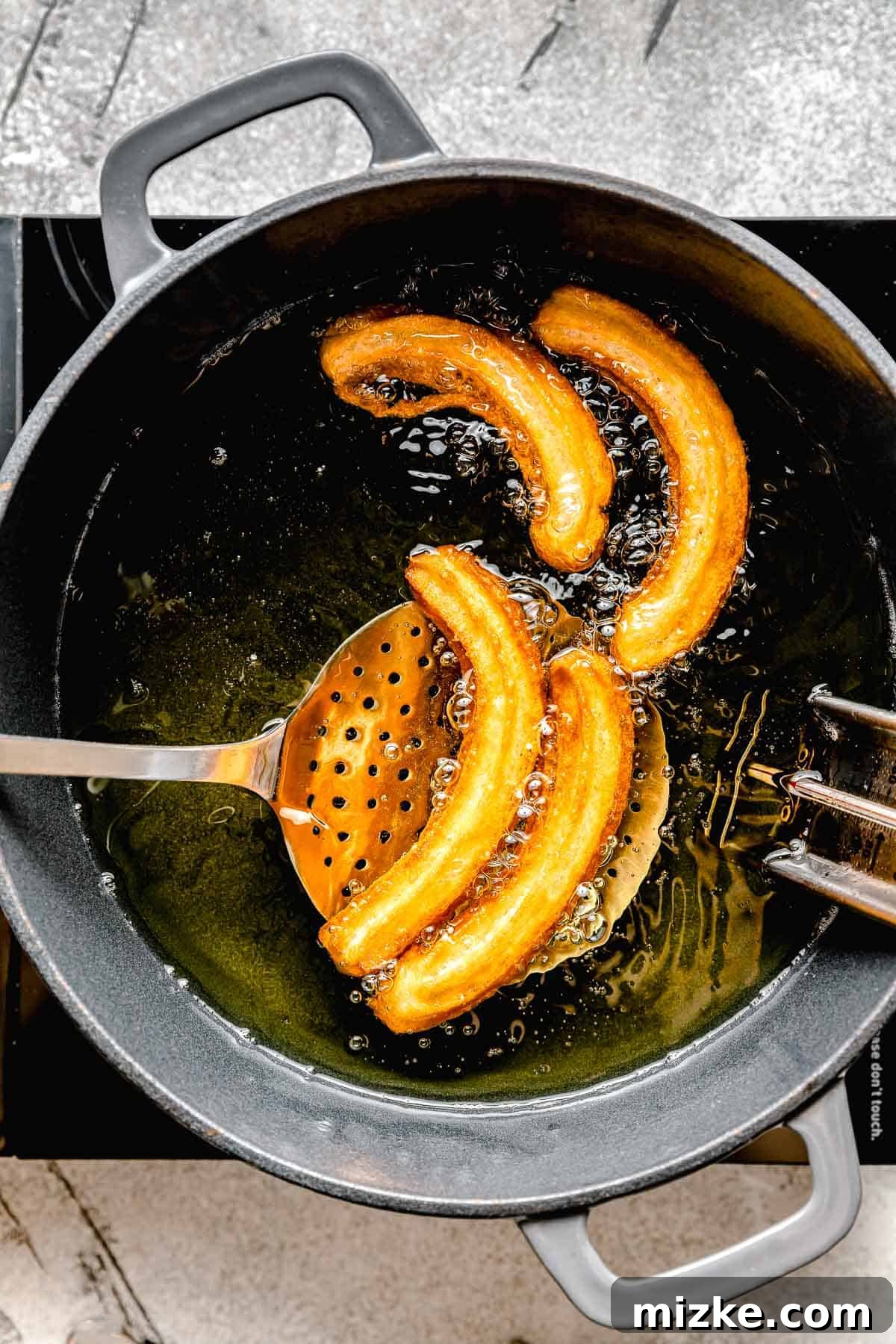 fried churros being scooped out of hot oil with a metal slotted spoon