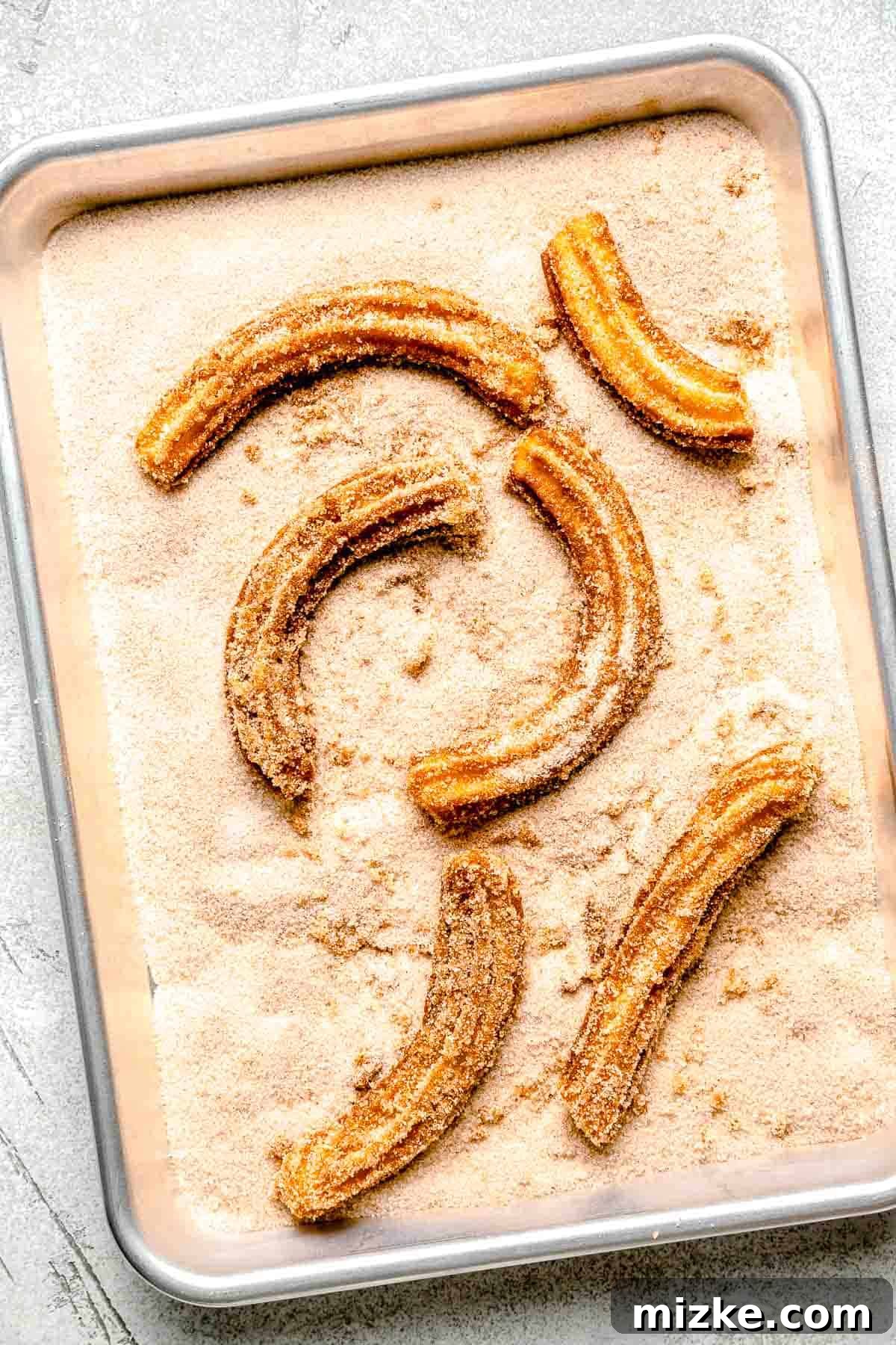 fried churros in cinnamon sugar on a metal baking sheet