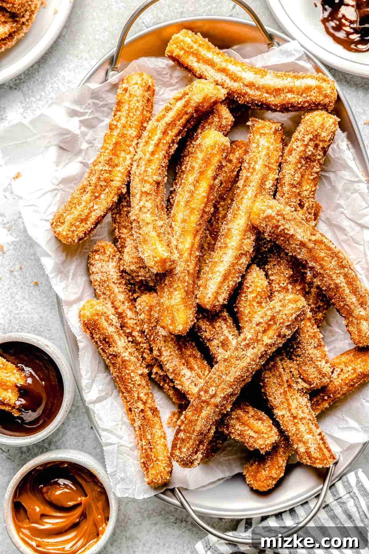 mexican churros on a metal platter next to dipping sauces