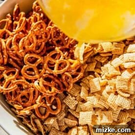 Butter mixture being poured over dry Chex cereal and pretzels in a bowl