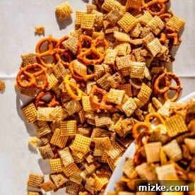 Homemade Chex Mix spread on a parchment-lined baking sheet, ready for the oven
