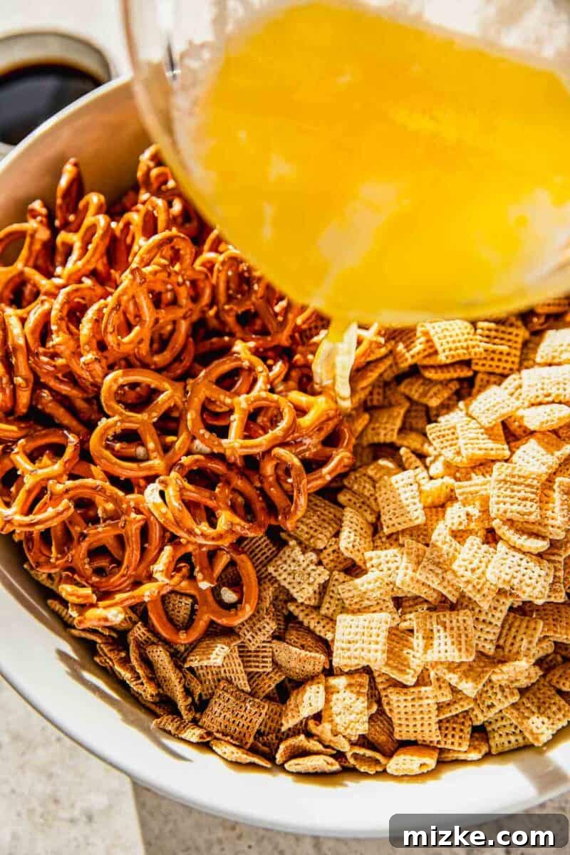 Irresistible Chex Crunch 6 The butter and seasoning mixture being poured over the dry Chex cereal and pretzels in a large bowl