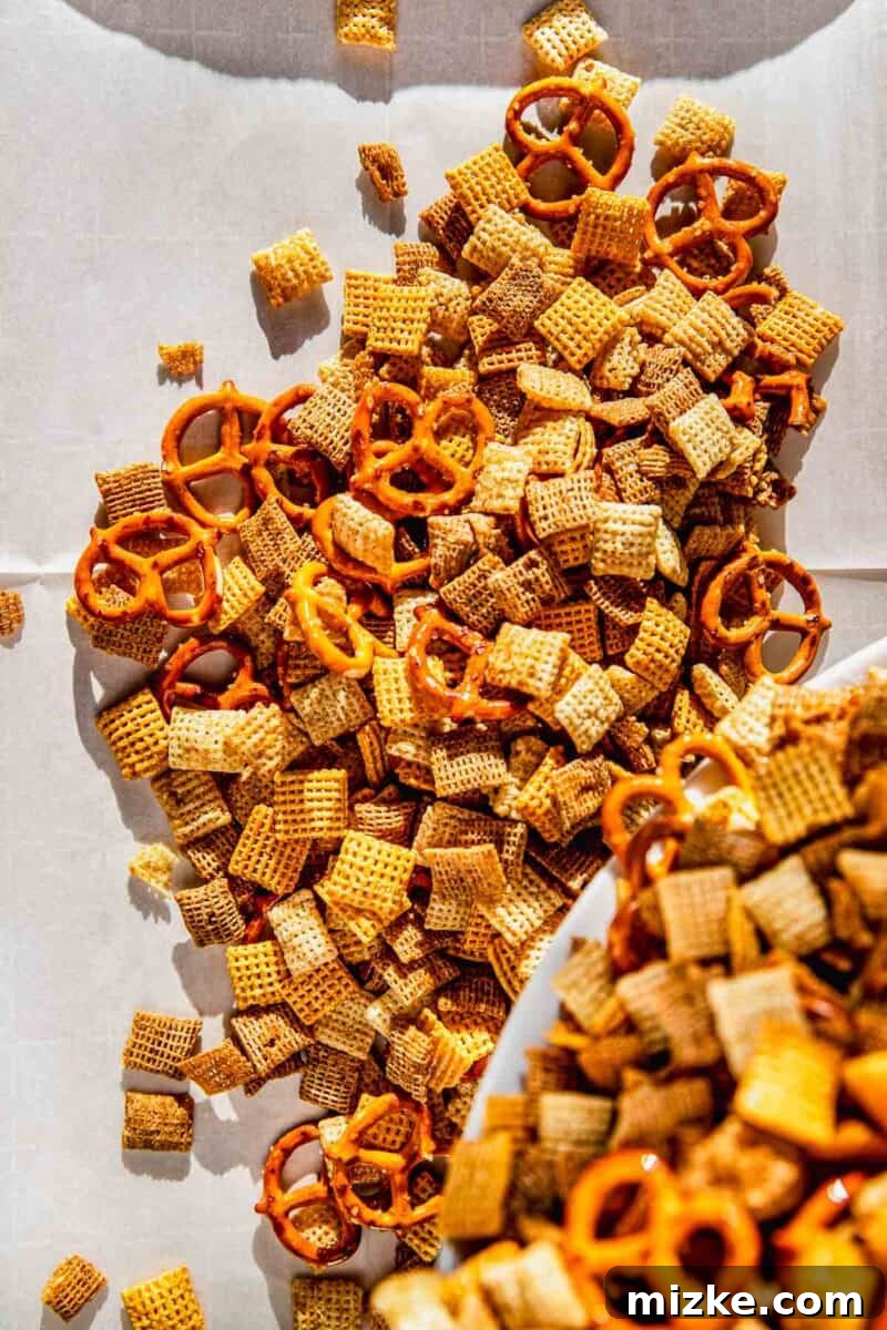 Irresistible Chex Crunch 7 Coated homemade Chex Mix being poured out onto a parchment-lined baking sheet in an even layer