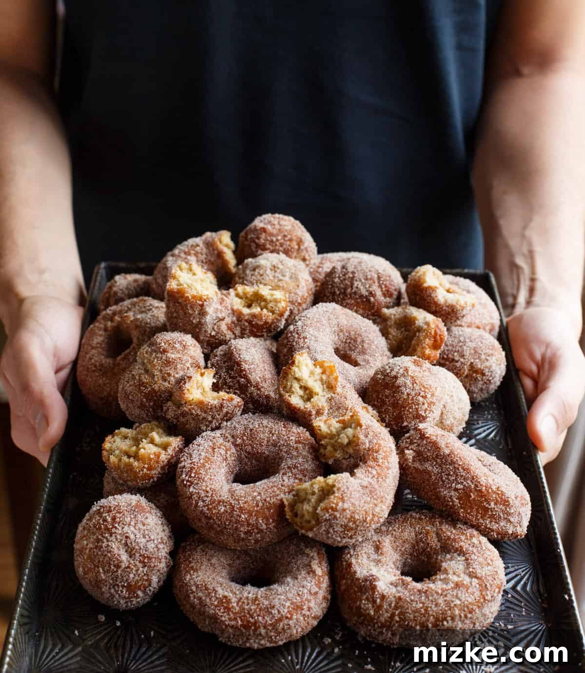 Spiced Apple Cider Doughnut Delights 2 Person holding baking sheet full of homemade apple cider doughnuts, symbolizing the joy of fall baking