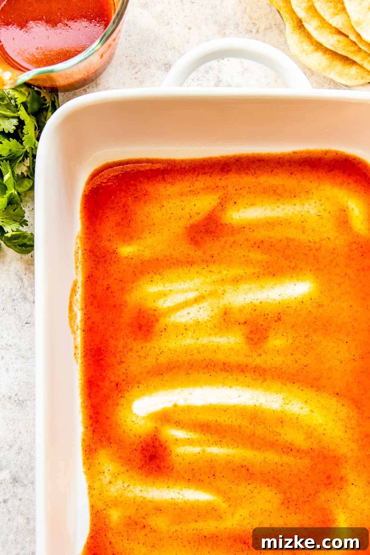 Effortless Homemade Chicken Enchiladas 3 A vibrant red enchilada sauce is expertly spread across the bottom of a white ceramic baking dish, creating a flavorful base for the easy chicken enchiladas.