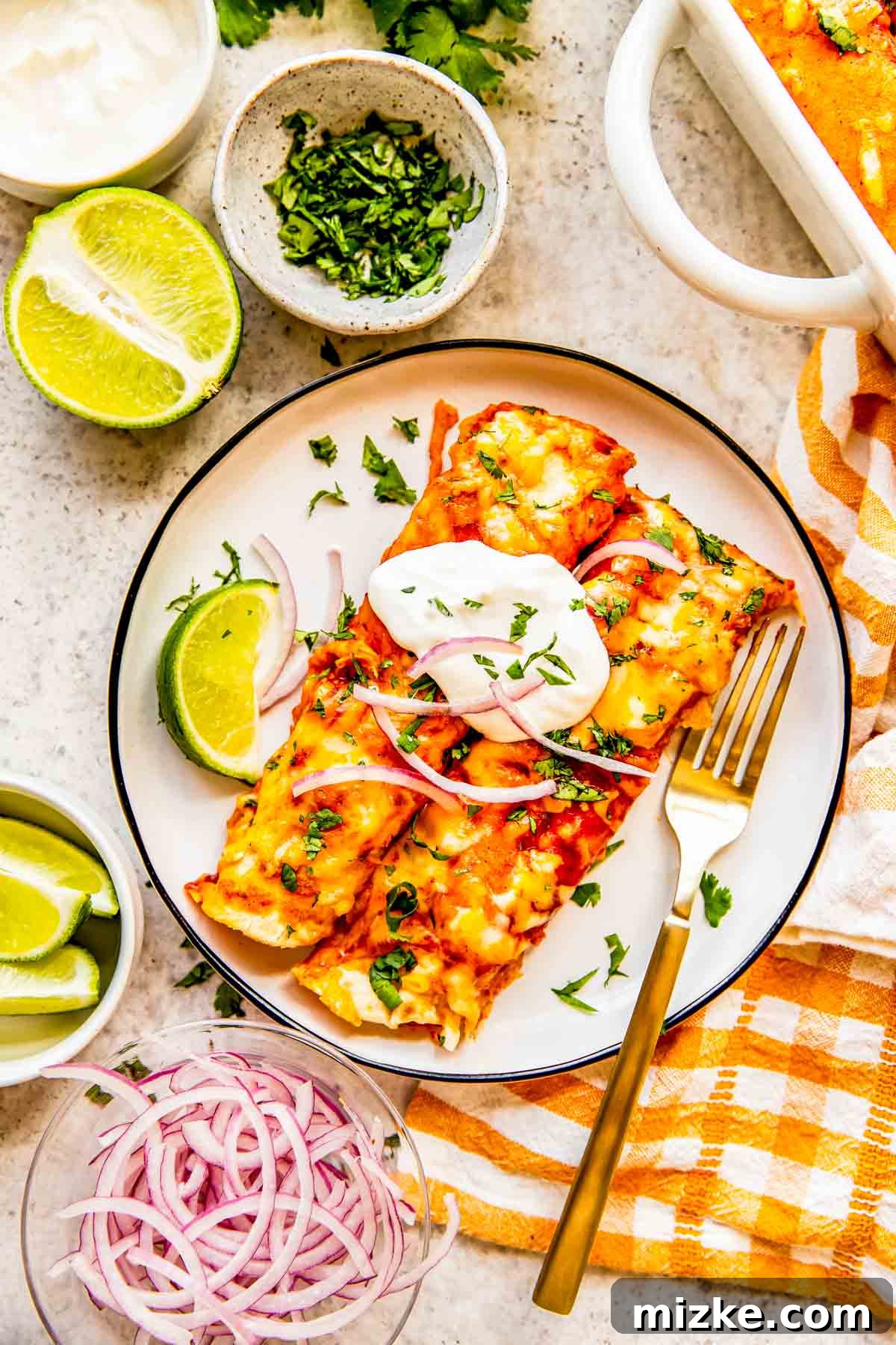 Effortless Homemade Chicken Enchiladas 8 Two perfectly baked chicken enchiladas, topped with a dollop of sour cream, a sprinkle of fresh cilantro, and vibrant pickled red onions, served on a white plate with a lime wedge and a fork, ready to be enjoyed.