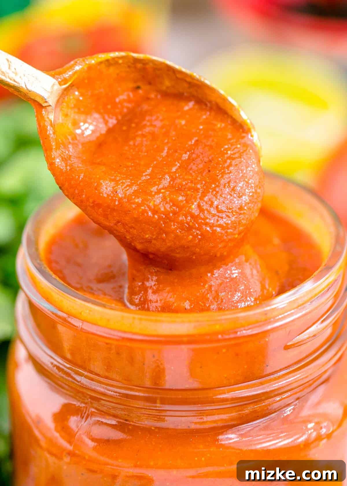 Easy Blender Red Enchilada Sauce 4 A spoon dips into rich red enchilada sauce in a glass jar, highlighting its inviting texture and color