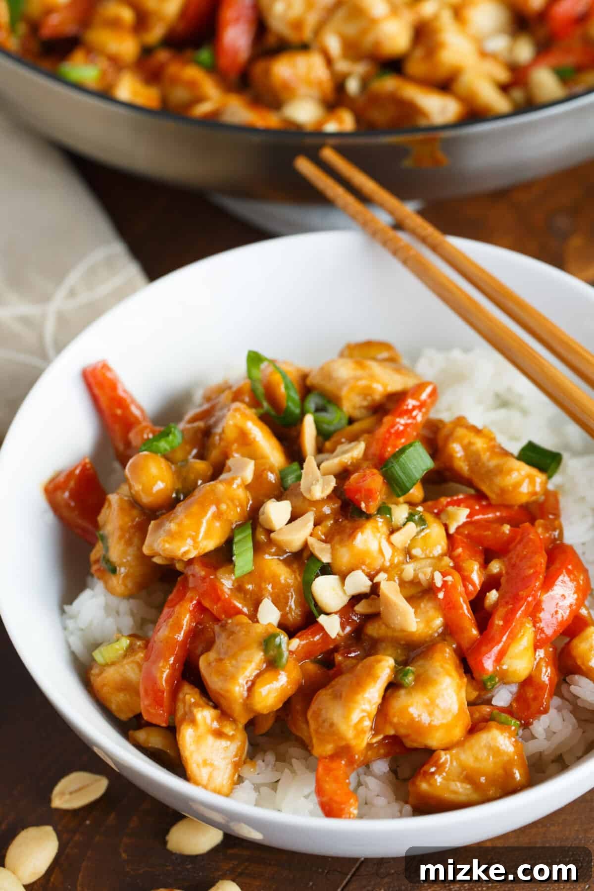 Spicy Peanut Chicken Stir-fry 3 Spicy peanut chicken served on a bed of white rice in a white bowl, with wooden chopsticks resting on the side.