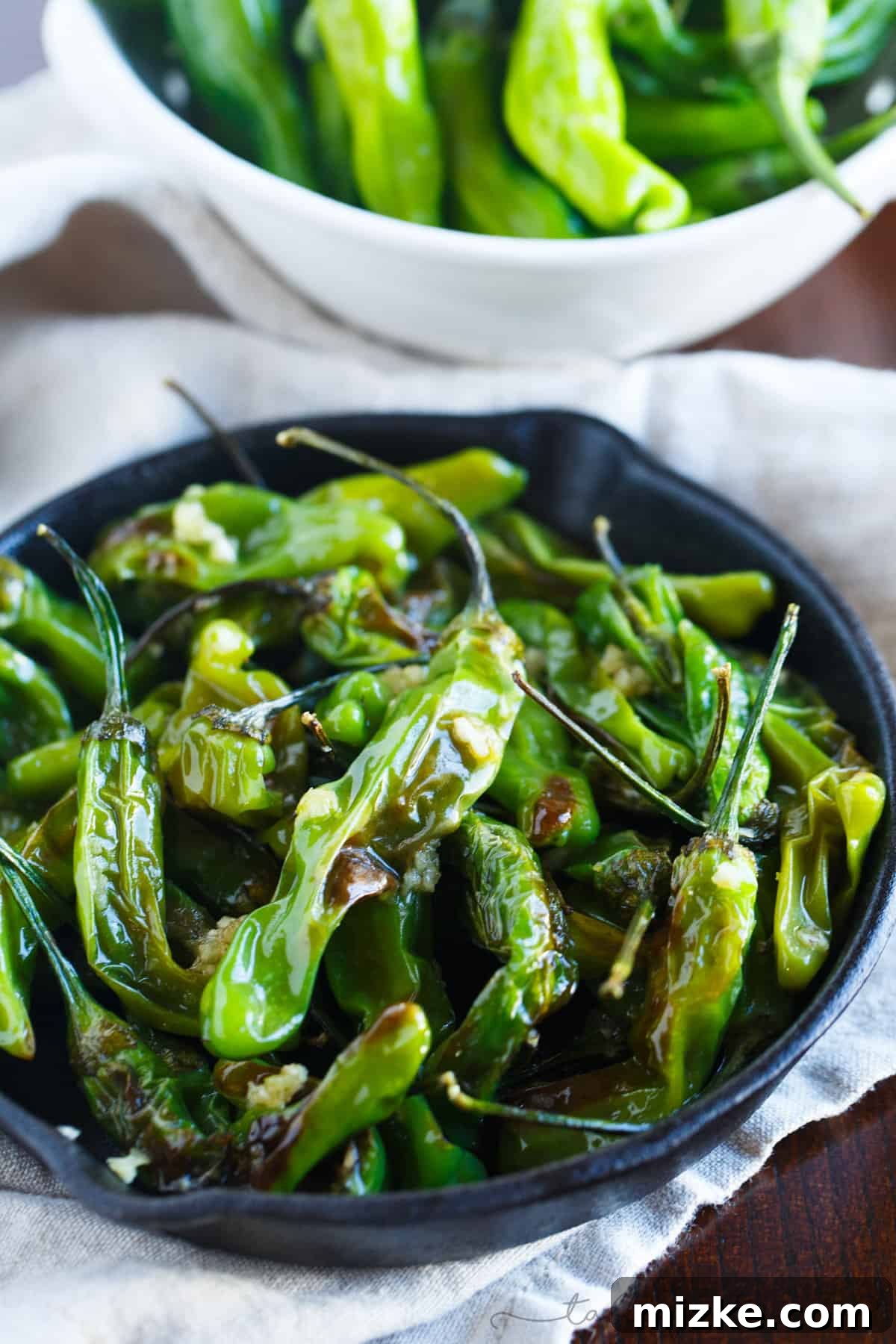 A tantalizing plate of blistered shishito peppers, glistening with olive oil and garlic, ready to be enjoyed as a snack.