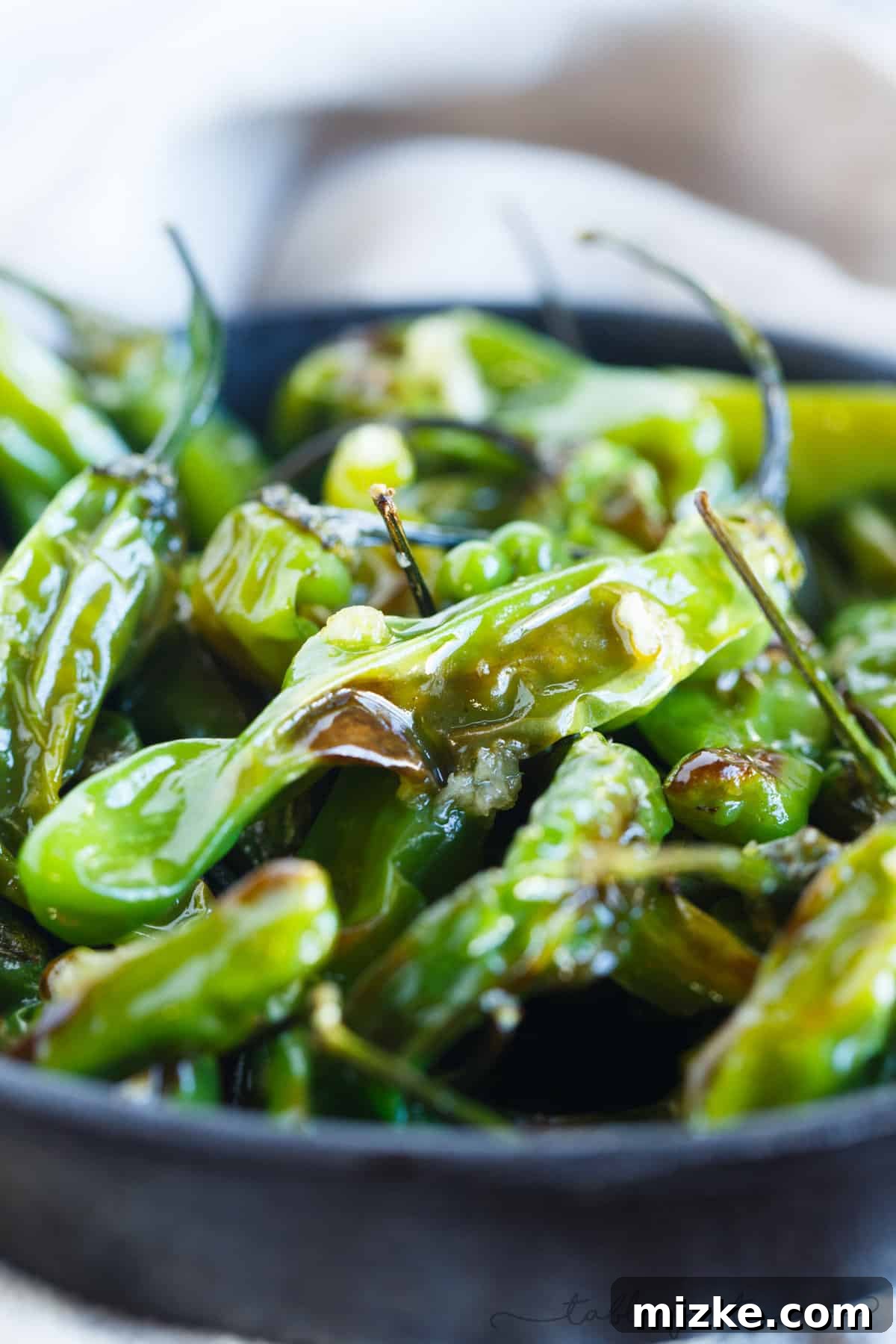 A close-up view of blistered shishito peppers in a bowl, tossed with fragrant minced garlic.
