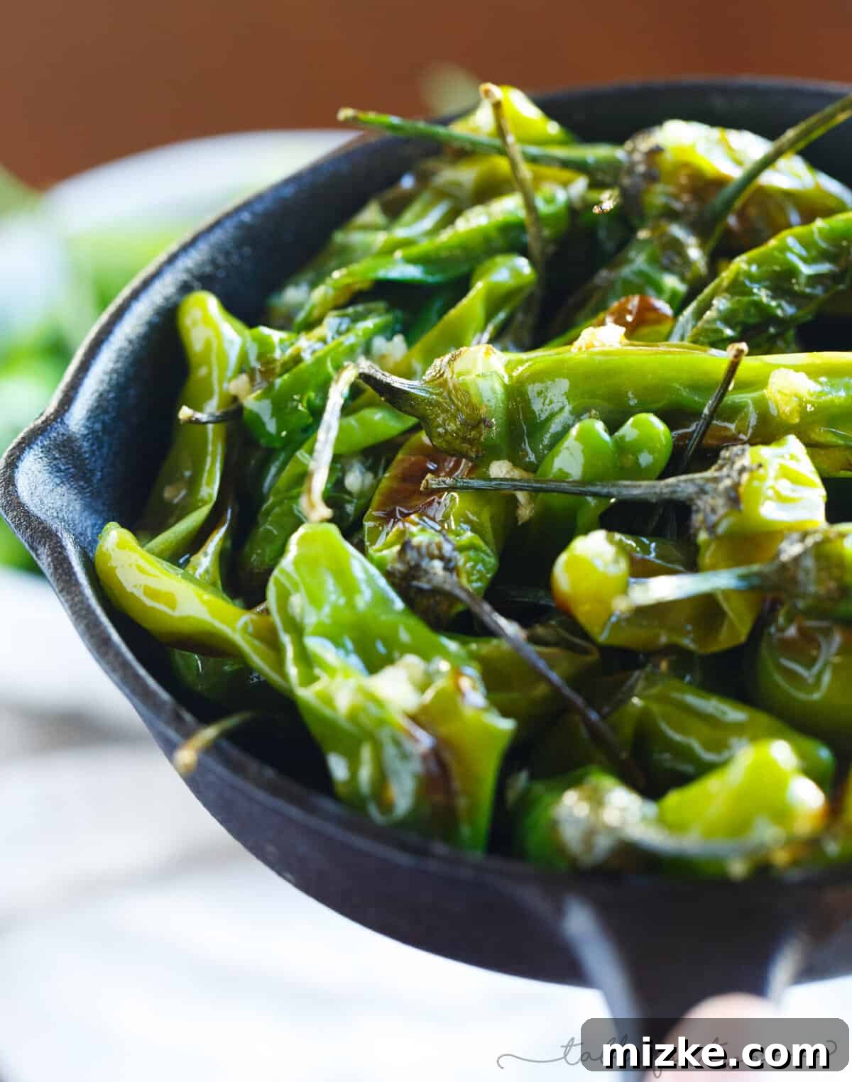 A hand reaching for a blistered shishito pepper, symbolizing the irresistible appeal of this easy-to-make snack.