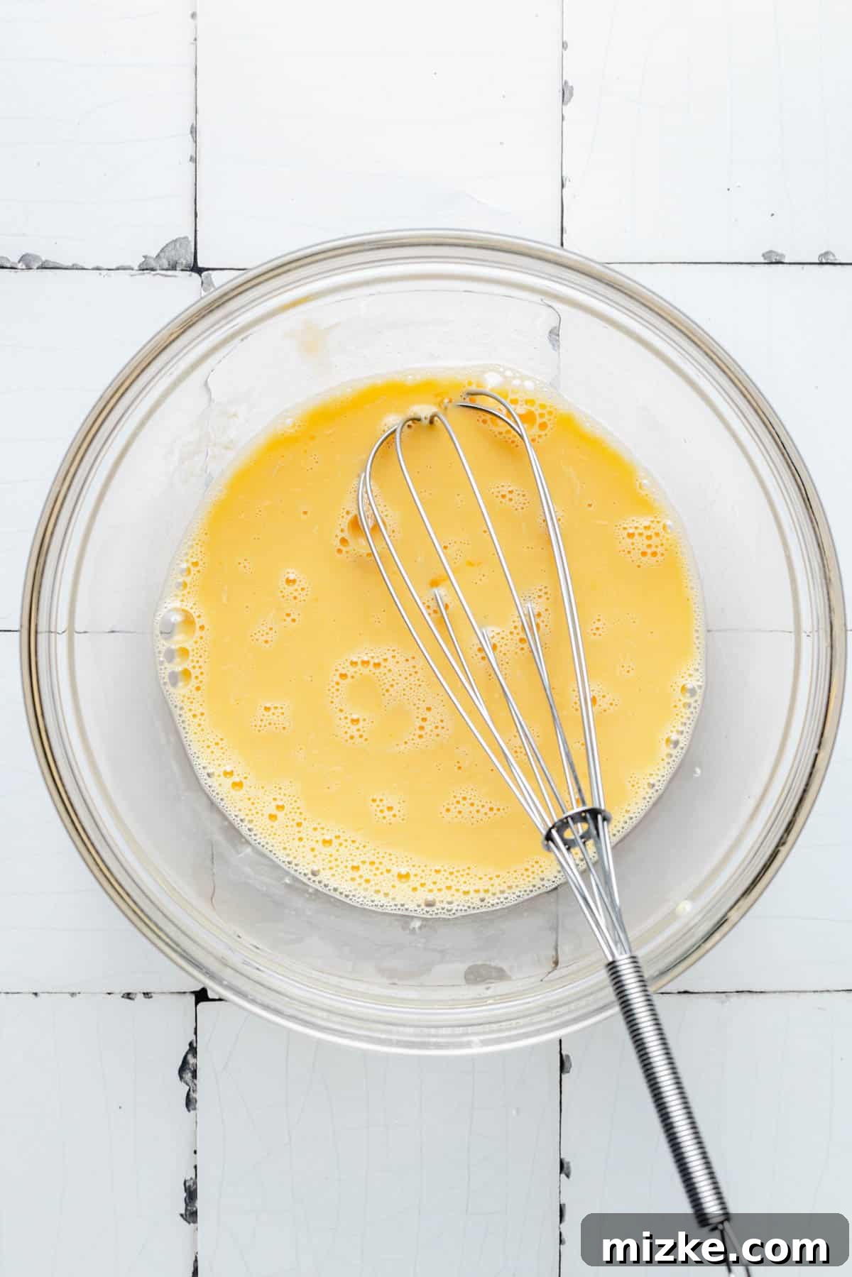 A bowl of wet ingredients, including milk, eggs, and extracts, being whisked together smoothly.