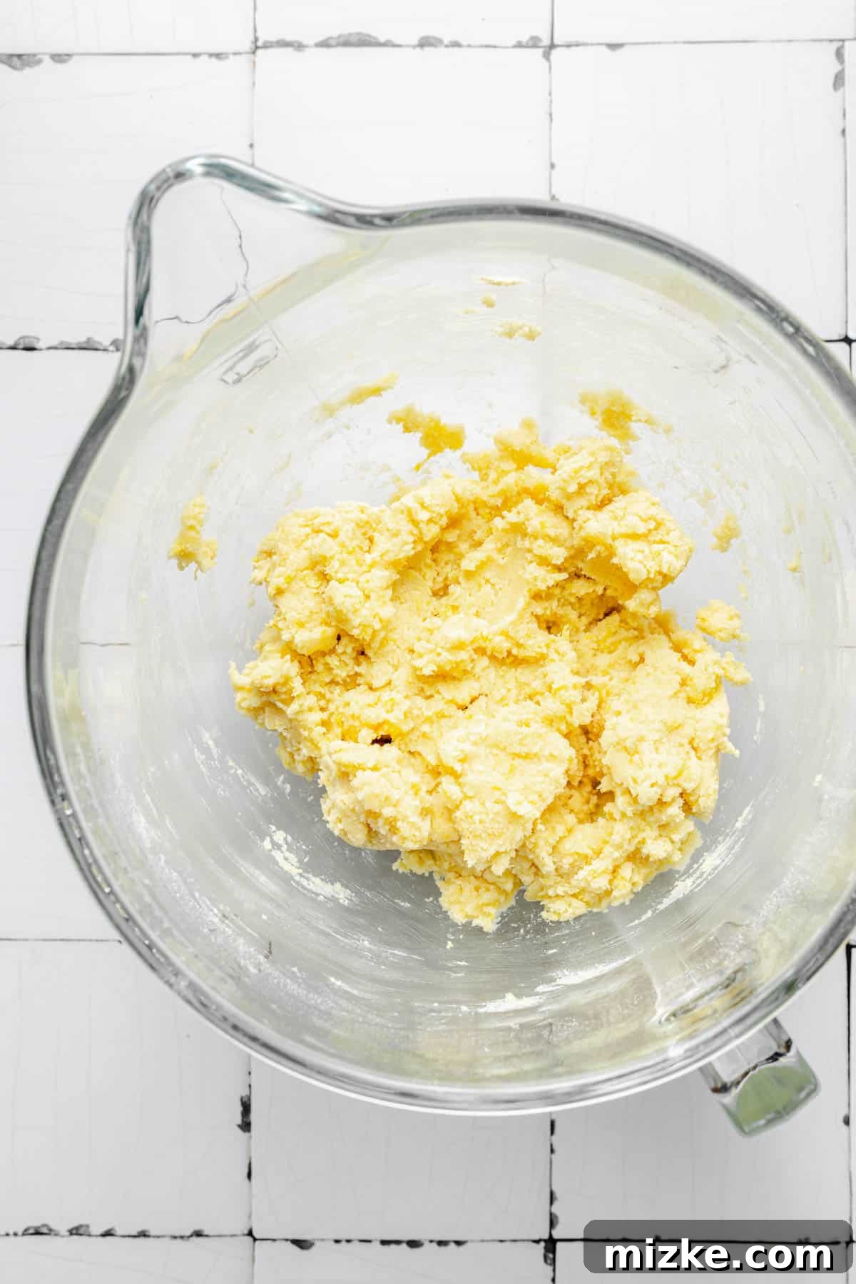 A butter mixture in a glass mixing bowl with dry ingredients, illustrating the initial stage of combining them.
