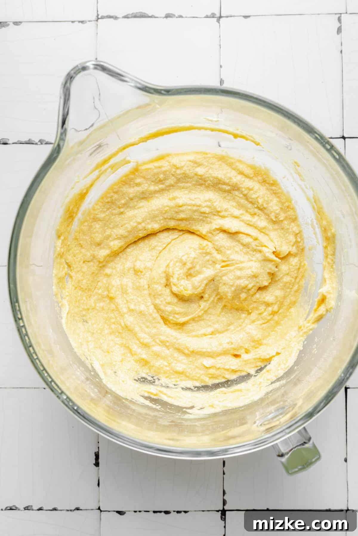 Smooth, light yellow cake batter is presented in a clear glass mixing bowl, ready for baking.