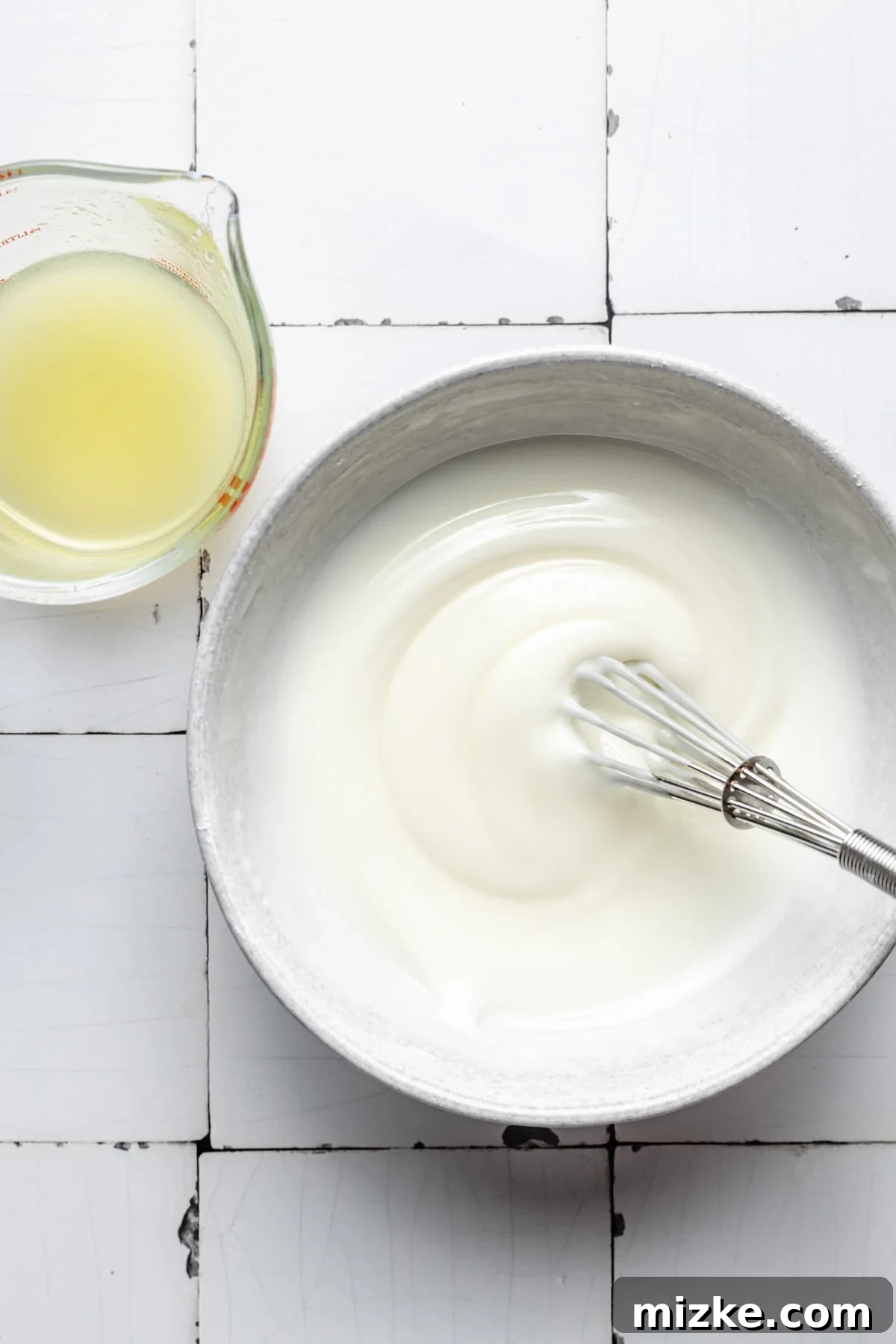 Thick, white lemon icing is being whisked in a bowl, showing its creamy texture.