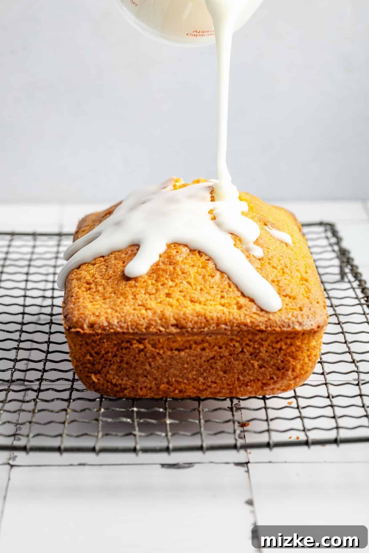 Thick, white lemon icing is being artfully drizzled on top of a freshly baked lemon pound cake, creating an inviting visual.