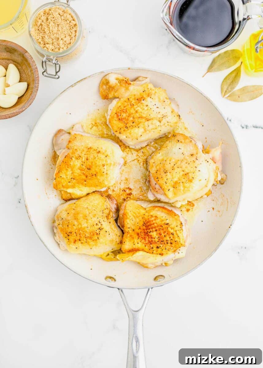 browned and seared bone-in, skin-on chicken thighs in a white nonstick skillet