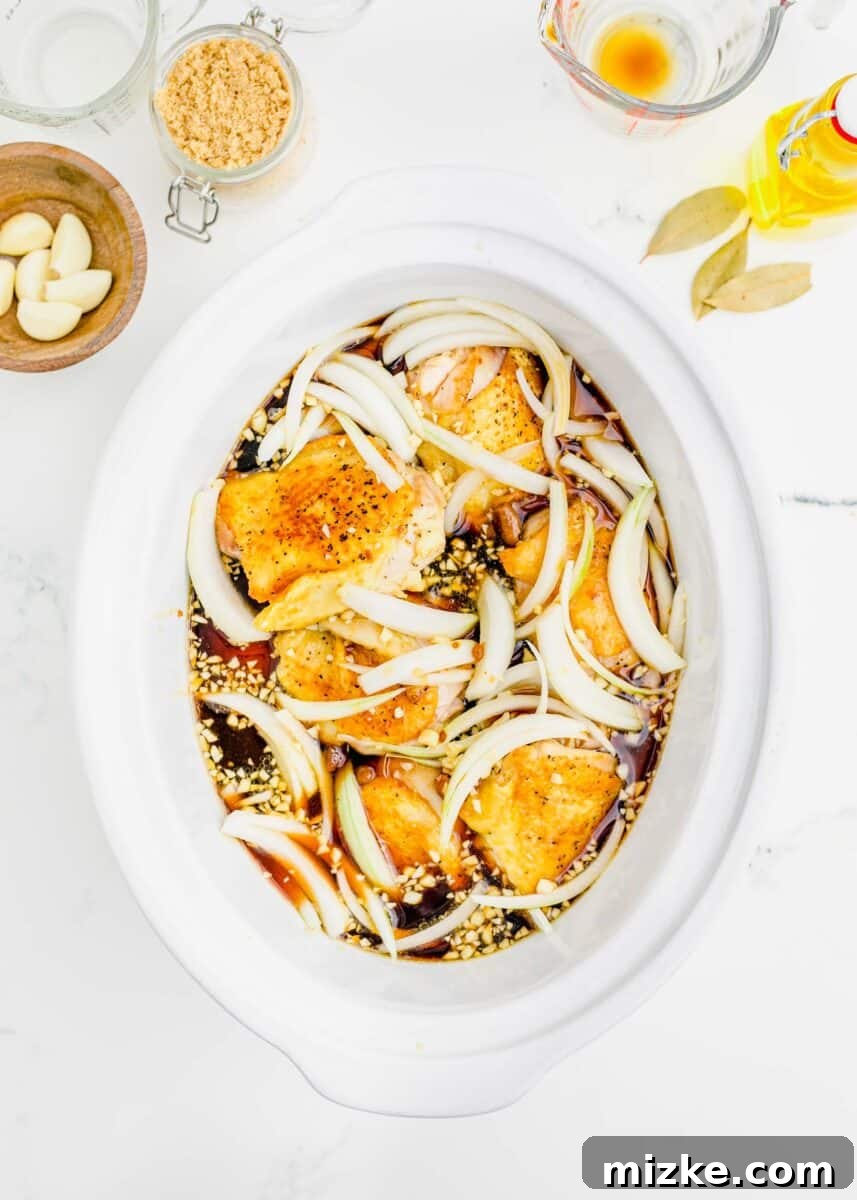 raw onions sprinkled on top of the seared chicken thighs in the slow cooker insert