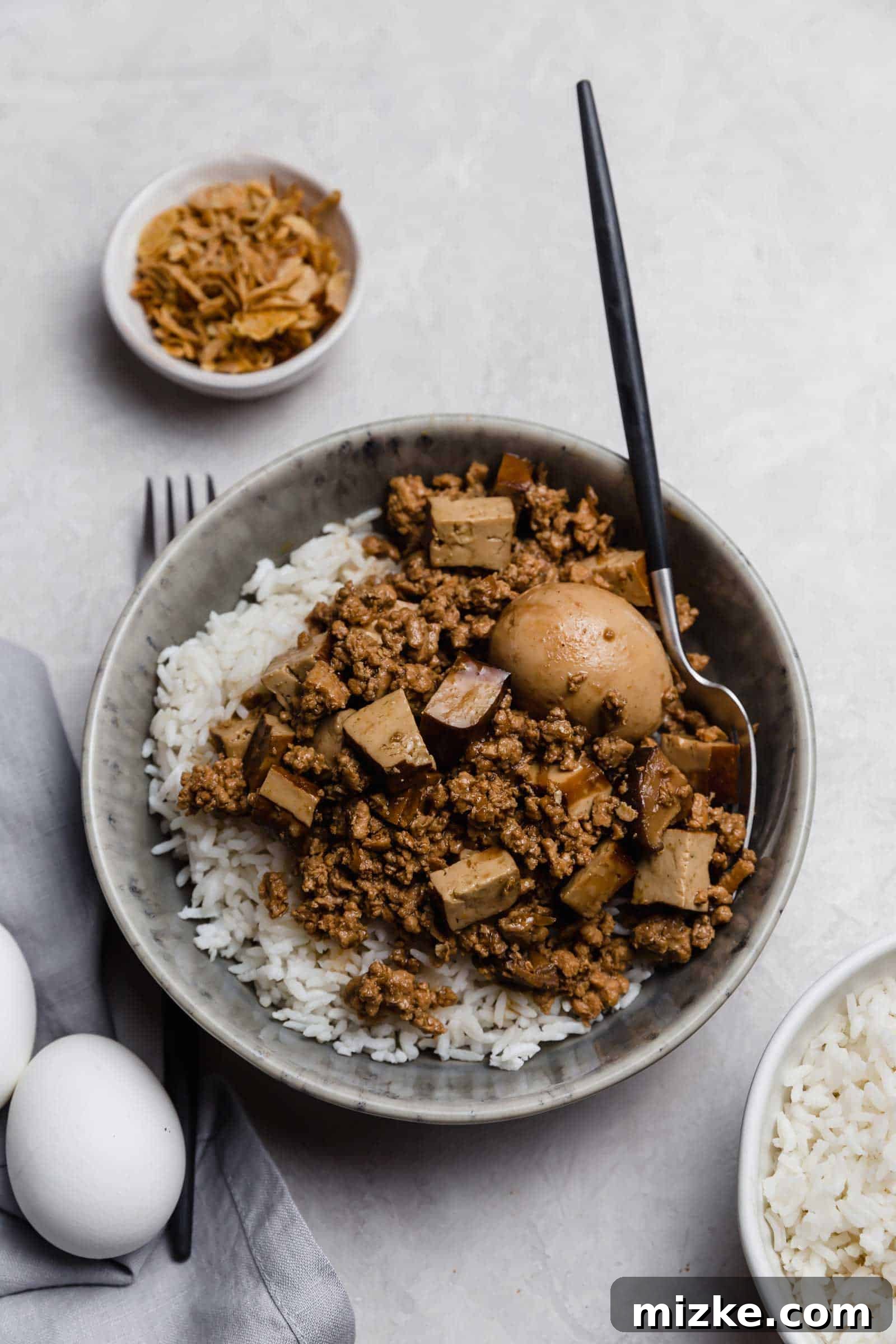 Taiwanese braised minced pork served with a delicious braised hard-boiled egg. A close-up of a serving of Taiwanese Braised Minced Pork (Lu Rou Fan) in a rustic bowl, garnished with a perfectly halved braised hard-boiled egg, highlighting the rich, glossy sauce and tender pork.