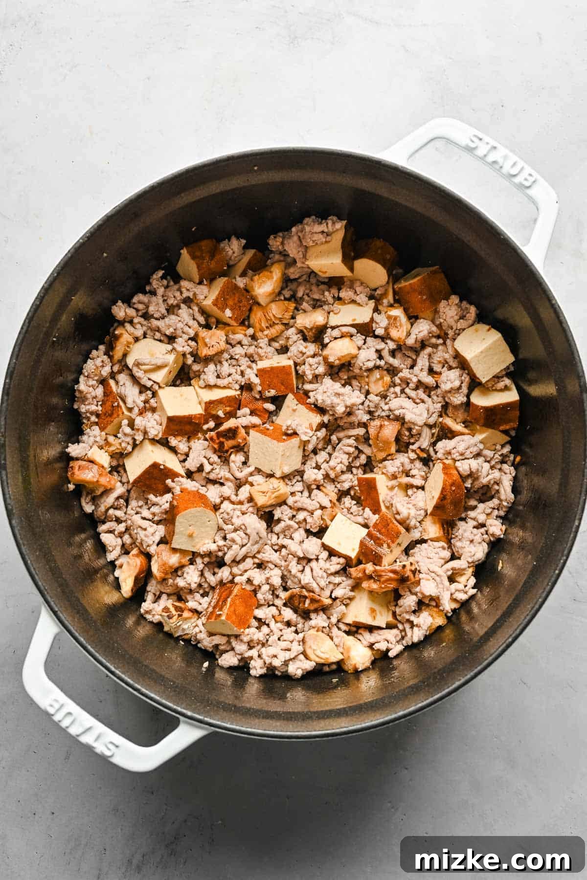 Combining ground pork with shiitake mushrooms, tofu, and fried scallions for Ro Zao. Ground pork being cooked in a large pot, with diced shiitake mushrooms, tofu, and fried scallions already added and mixing into the savory braise.
